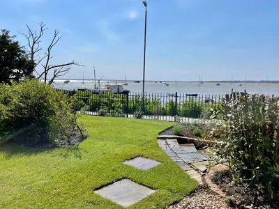 a yard with a grassy yard with a body of water at Cosy Coastal 2-Bedroom Cottage with Hot Tub and Log Burner in West Mersea