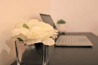 a vase with white flowers sitting on a desk with a laptop at Lovely Modern Apartment Close to Town Centre in Lexden