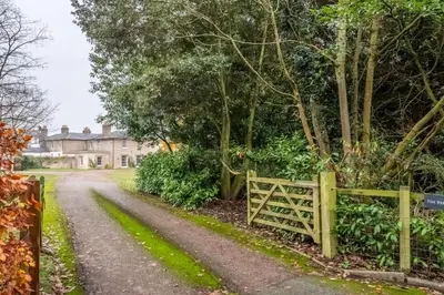 a fence in front of a house with a driveway at Bell Tower Cottage in Middleton