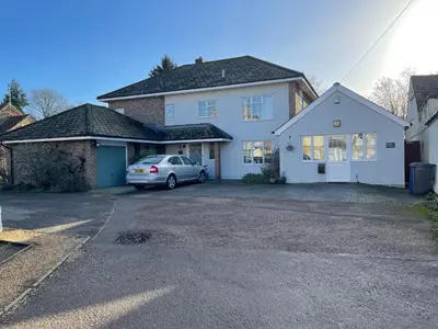 a white house with a car parked in a driveway at Silver Lodge Guest House in Mildenhall