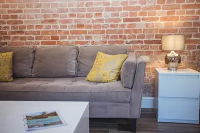 a living room with a couch and a brick wall at Lynford Holiday Cottages nestled in the heart of Thetford Forest in Mundford