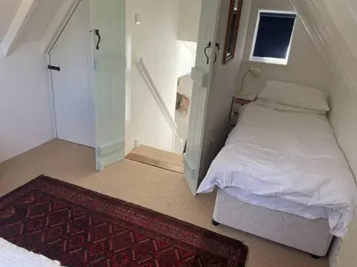 a small bedroom with a bed and a staircase at Acacia Cottage in Halstead