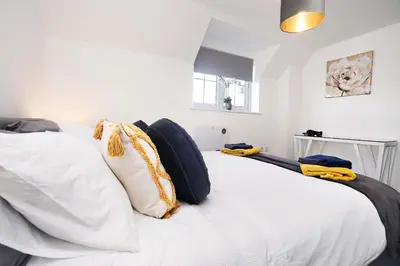 a bedroom with a white bed with black and yellow pillows at Victoria Gardens in Colchester