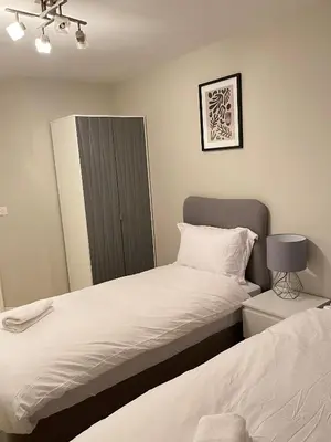 a bedroom with two beds and a cabinet and a mirror at Next-Stop Haven in Harlow