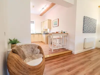 a living room with a chair and a kitchen at Feathers, Blythburgh in Halesworth