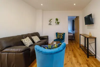 a living room with a leather couch and a blue chair at Three Tuns - Garden Suite 2 in Wickham Market