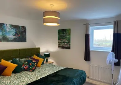 a bedroom with a bed with colorful pillows and a window at Contemporary, Cosy & Homely 2 Bed Apartment with High-Speed WIFI, Terrace & Free Parking overlooking Stourbridge Common Park & Coldham's Brook in Cambridge
