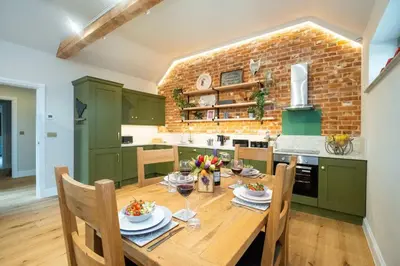 a kitchen with a wooden table with glasses of wine at Alde Bay Farm - Coral Cottage in Aldeburgh