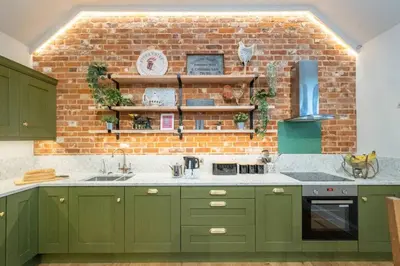 a kitchen with green cabinets and a brick wall at Alde Bay Farm - Coral Cottage in Aldeburgh