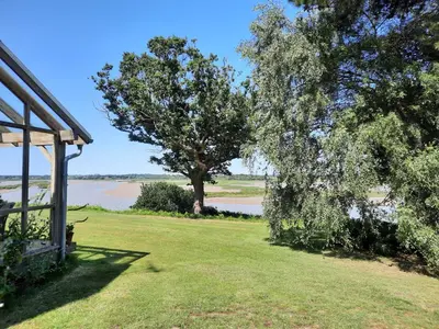 a house with a tree next to a body of water at River View - Stunning estuary views in Aldeburgh