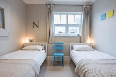 two beds with a blue chair in a room at 3 St Nicholas Court, Aldeburgh in Aldeburgh