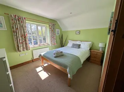 a green bedroom with a bed and a window at Rockhopper Cottage, Waldringfield in Woodbridge