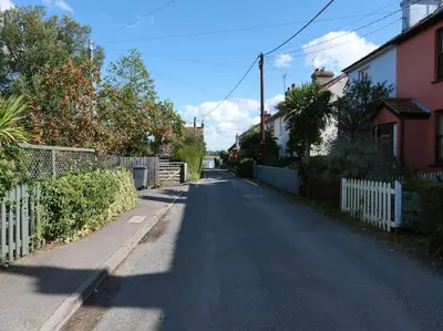 an empty street with a white fence and houses at Rockhopper Cottage, Waldringfield in Woodbridge