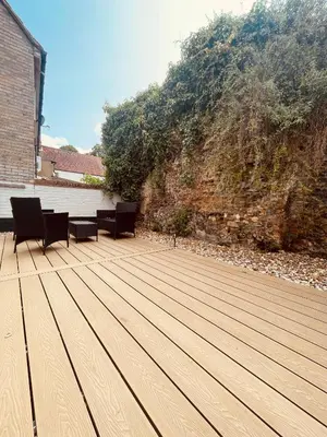 a wooden deck with two chairs and a wall at Abbey Gardens Cottage in Bury Saint Edmunds