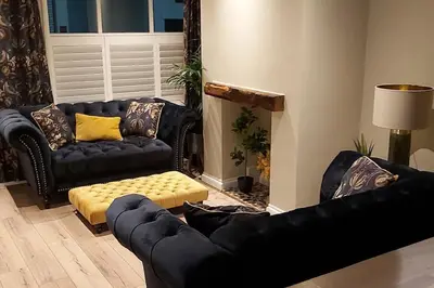 a living room with black leather couches and a yellow stool at Stylish Town House in Medieval Grid in Bury Saint Edmunds