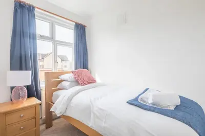a bedroom with a bed with blue curtains and a window at Charming Central Family Home in Cambridge