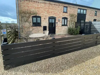 a fence in front of a house with a table at Pretty Cottage In Charming Peaceful Village - Easy Commute to Cambridge - Cambridge Homehost in Cambridge
