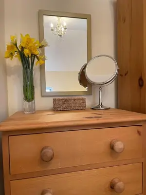 a vase of yellow flowers and a mirror on a dresser at Pretty Cottage in peaceful village location close To Cambridge in Cambridge