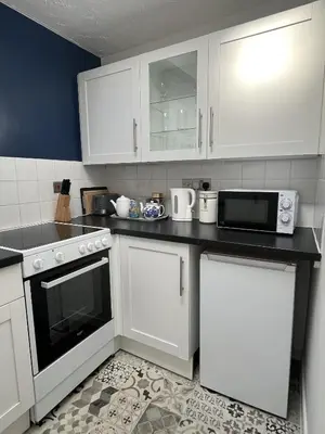 a kitchen with white cabinets and a black counter top at Windmill Cottage in Ely