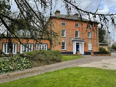 an old brick building with white windows and a driveway at Lydney House Hotel Swaffham Sleeps 22 in Swaffham