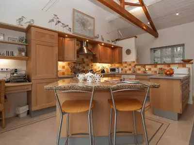 a kitchen with wooden cabinets and a island with bar stools at Valley Farm Cottage in Woodbridge