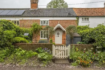 a brick house with a white gate and flowers at Well Green Cottage in Wenhaston