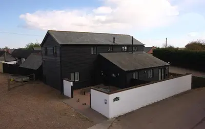 a black house with a white wall next to it at The Cart Lodge at Lee Wick Farm Cottages & Glamping in Saint Osyth
