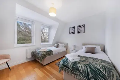 a bedroom with two beds and a chair and two windows at Roomy One bed loft apartment in Bishops Stortford