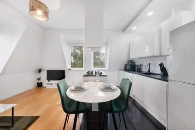 a white kitchen with a table and green chairs at Roomy One bed loft apartment in Bishops Stortford