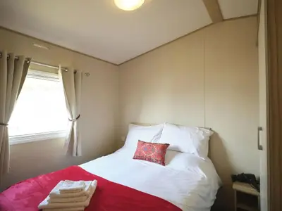 a bedroom with a bed with a red pillow and a window at Lighthouse Holiday Retreat in West Mersea