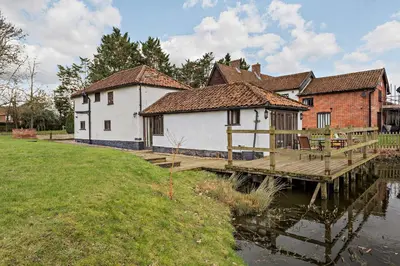 a house on a dock next to a body of water at Amazing Spa Country House with Indoor Pool, Sauna and Steam Room in Tibenham