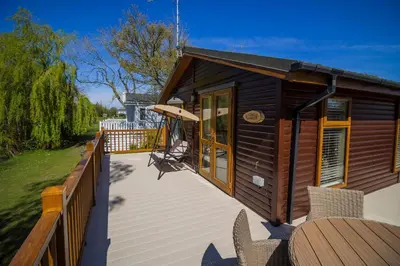 a wooden cabin with a deck with chairs on it at Stunning Lodge For Hire At Carlton Meres In Suffolk Ref 60013M in Saxmundham
