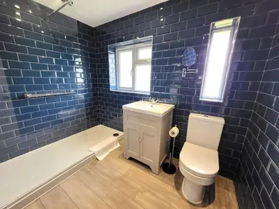 a blue tiled bathroom with a toilet and a tub at Jersey Cottage in Horseheath