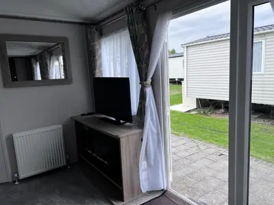 a living room with a sliding glass door with a television at Coopers Beach 3-Bed Caravan Sleeps 8 & Pets Ok in Colchester