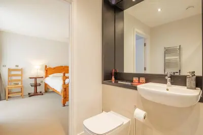 a bathroom with a sink and a toilet and a bedroom at Luxury Ensuite Room 2 Minutes from Cambridge Station in Cambridge
