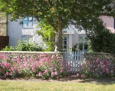 a white fence in front of a house with pink flowers at 2 Bed in Snape oc-sfbox in Snape