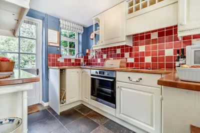 a kitchen with white cabinets and red tiles on the wall at 1 Bed in Yoxford oc-c27254 in Wickham Market