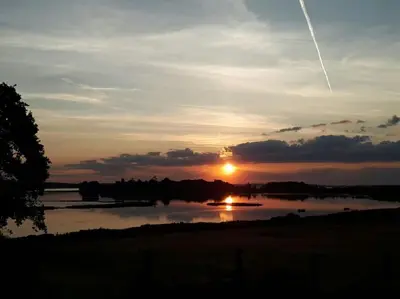 a sunset over a lake with a plane in the sky at River Cottage - Stunning estuary views in Aldeburgh