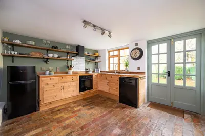 a large kitchen with wooden cabinets and black appliances at Buttercup Cottage, Hartest in Hartest