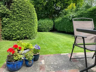 a garden with three potted plants and a chair at Buttercup Cottage, Hartest in Hartest
