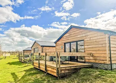 a wooden house with a deck on a field at Old Buckenham Country Park in Old Buckenham