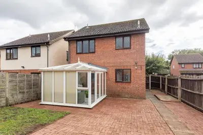 a red brick house with a white greenhouse in front of it at House on cul de sac in Lakenheath